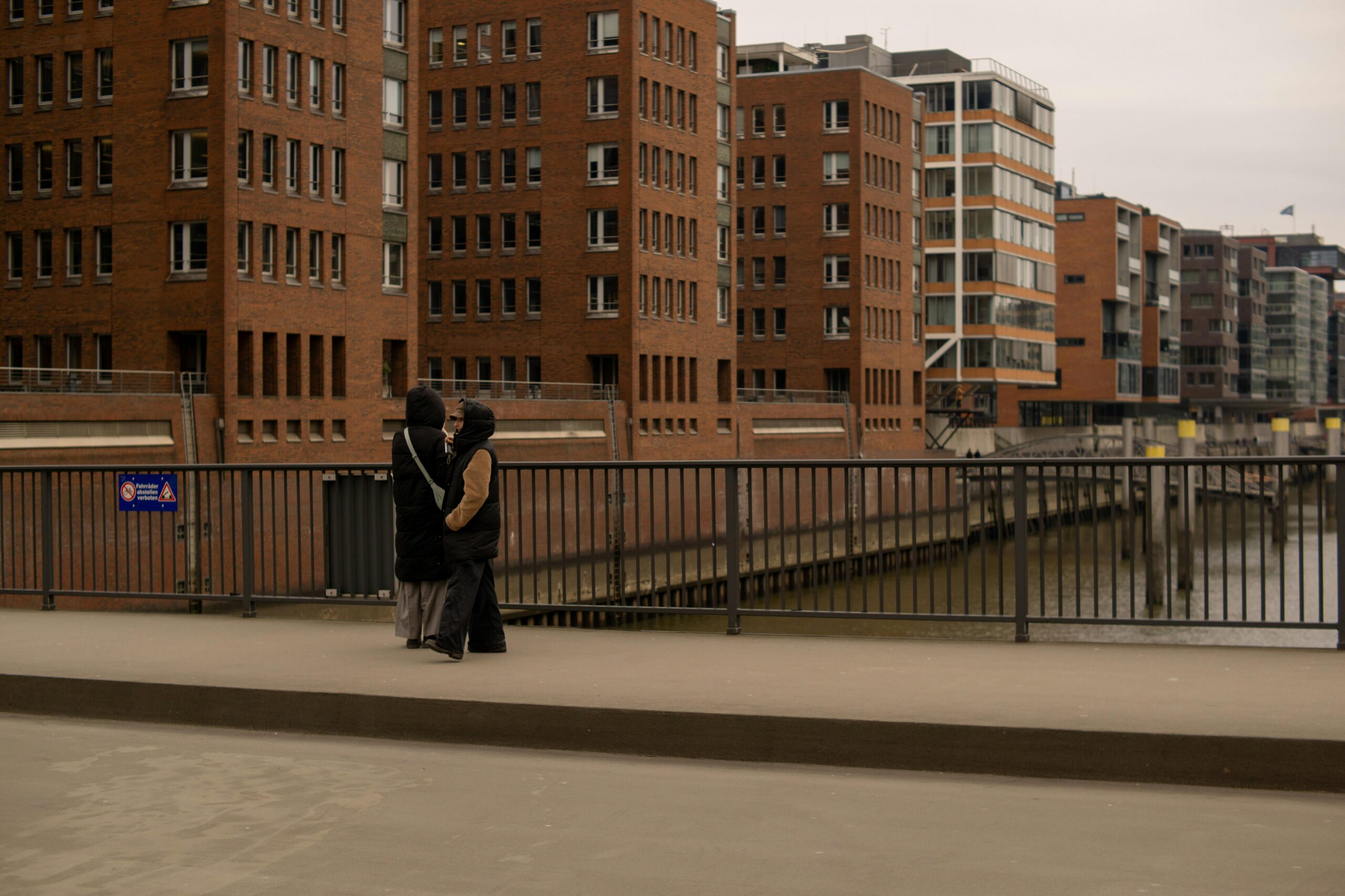 A couple standing by the river in Hamburg with brick architecture.