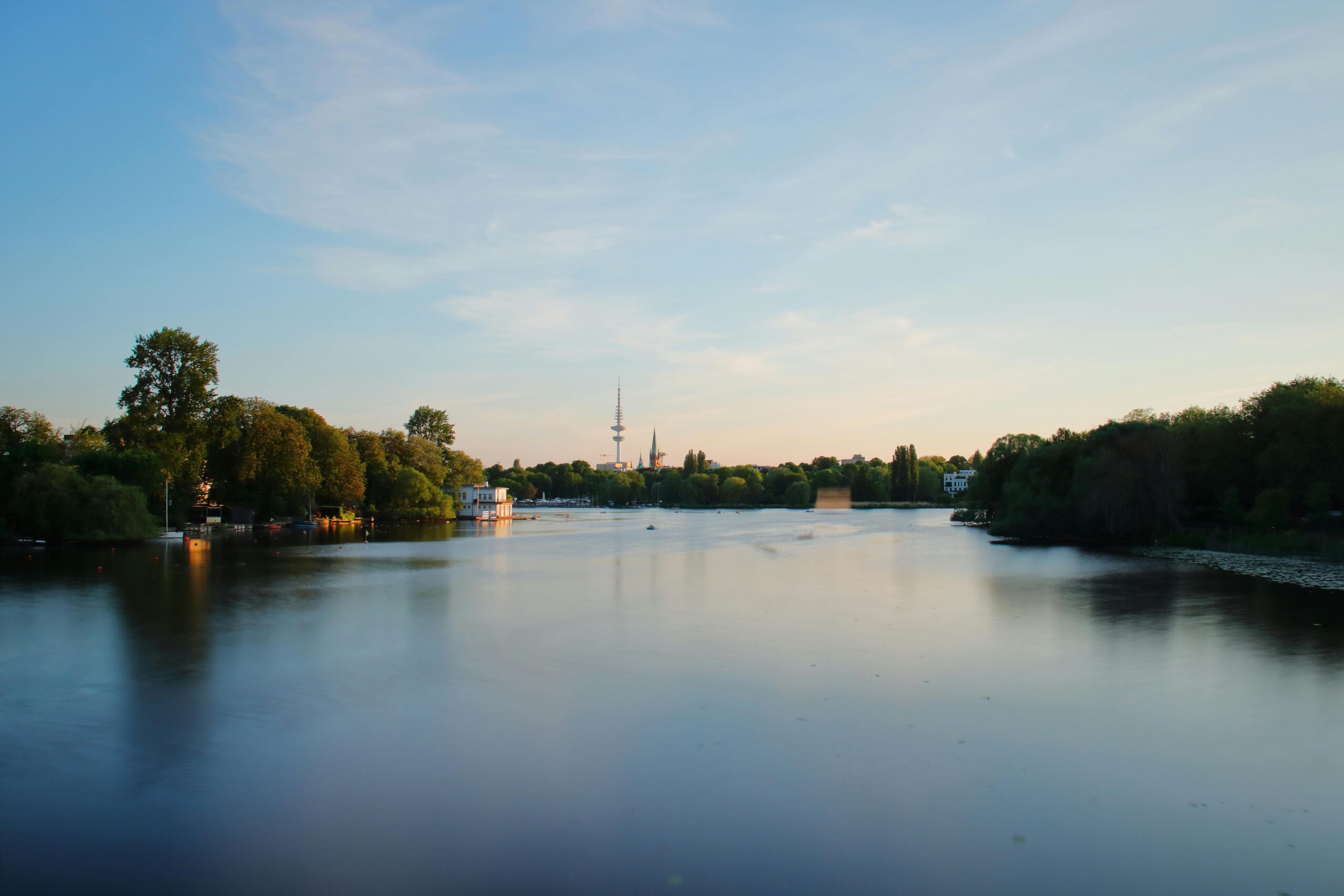Beautiful long exposure of the Alster River in Hamburg, Germany at sunset, highlighting nature and city skyline.