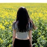 A woman stands in a vast field of yellow rapeseed flowers, enjoying the tranquil rural landscape.